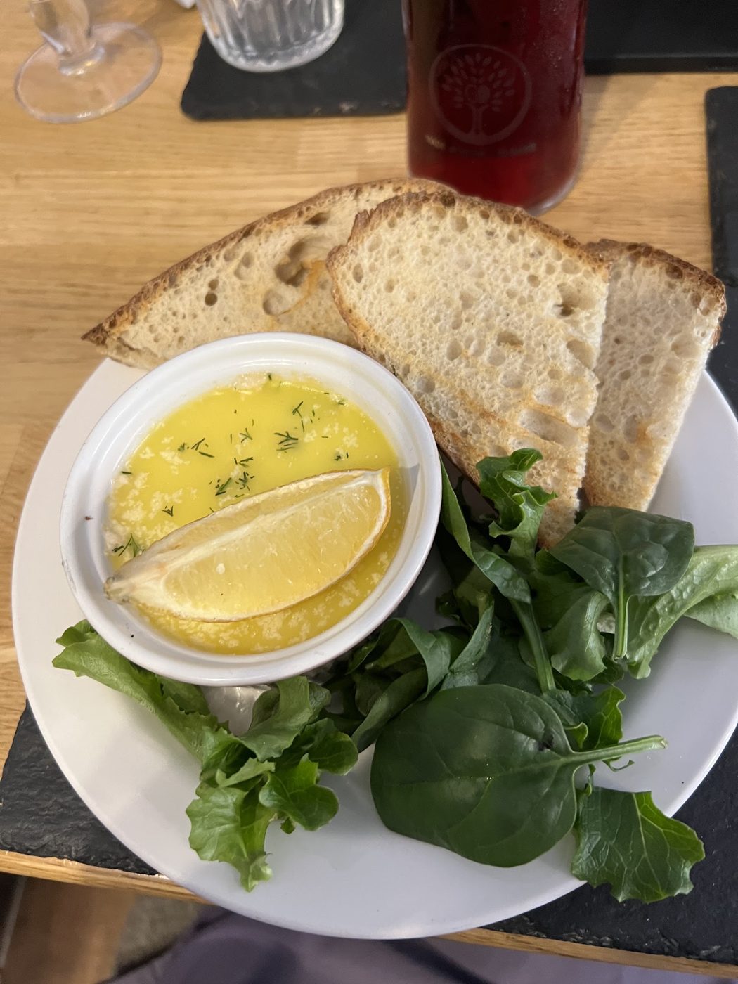 A bowl with a lemon wedge, bread and salad leaves