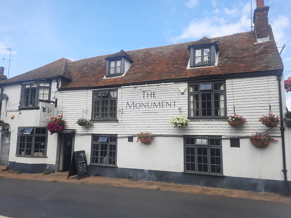 The white weatherboarded pub with THE MONUMENT lettering and hanging baskets